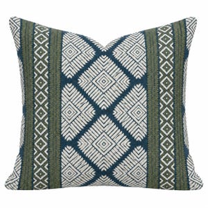 May include: A square throw pillow featuring a repeating geometric pattern of white diamonds and lines set against a deep blue background, accented by vertical bands of olive green with a textured, stitched appearance.