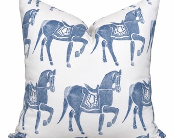 Puede incluir: Un cojín cuadrado con un patrón repetitivo de caballos azules sobre un fondo blanco. Cada caballo está representado en un estampado azul estilo acuarela, con silla de montar y brida, dispuestos en una cuadrícula sobre la superficie de la tela.