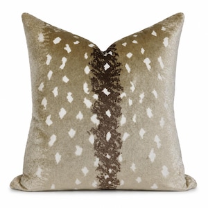 May include: A square throw pillow featuring a light tan base with a vertical dark brown textured stripe down the center. The surface is covered in a repeating pattern of small, irregular white spots that resemble a natural animal hide print.