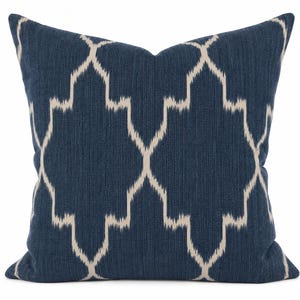 May include: A square throw cushion featuring a deep navy blue fabric base with a prominent, repeating off-white geometric ikat pattern. The textile has a visible woven texture, and the design consists of interconnected, elongated diamond shapes.