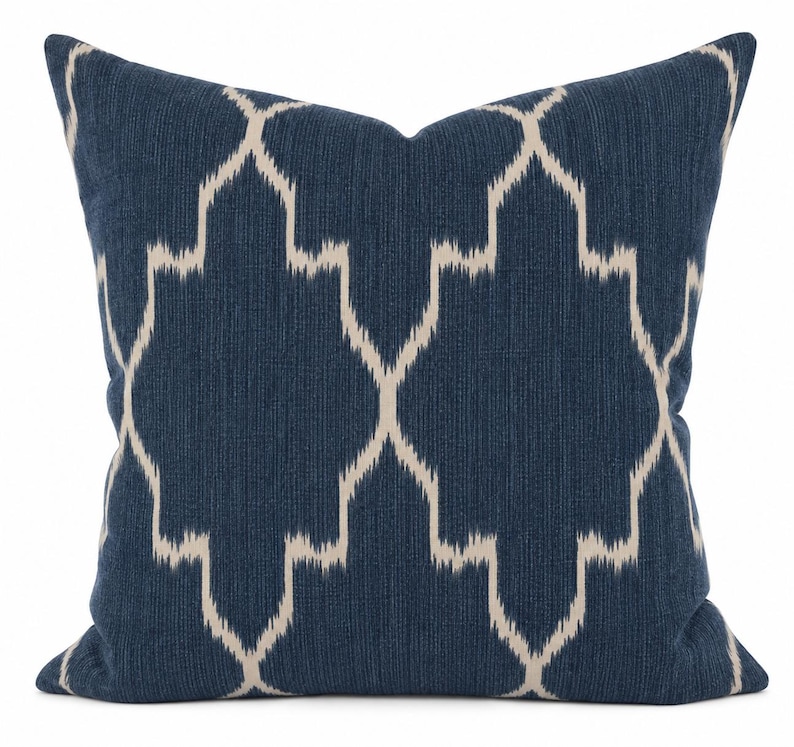May include: A square throw cushion featuring a deep navy blue fabric base with a prominent, repeating off-white geometric ikat pattern. The textile has a visible woven texture, and the design consists of interconnected, elongated diamond shapes.