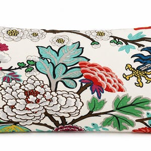 May include: A rectangular throw pillow with an off-white background featuring a colorful botanical print. The design includes large white and red peonies, green leaves, brown branches, a yellow lantern, and a blue bird with yellow talons.
