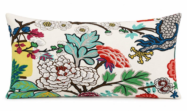 May include: A rectangular throw pillow with an off-white background featuring a colorful botanical print. The design includes large white and red peonies, green leaves, brown branches, a yellow lantern, and a blue bird with yellow talons.