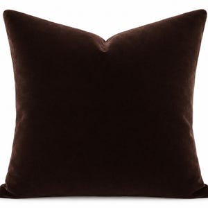 May include: A square throw pillow featuring a solid dark brown velvet fabric cover. The pillow has a distinct karate chop indentation at the top center, creating a soft, plush appearance with smooth, uniform texture across the entire surface.