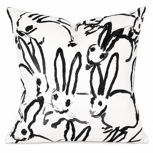 May include: A square throw pillow featuring a white background with a repeating black ink-style illustration of multiple rabbits. The design uses bold, expressive brushstrokes to depict the outlines and features of the various bunnies.