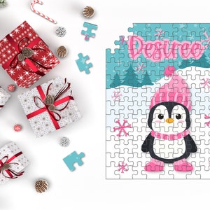 May include: A personalised jigsaw puzzle with a cartoon penguin in a pink hat and scarf, with the name "Desiree". The puzzle is surrounded by Christmas gifts, pine cones, and candy canes.