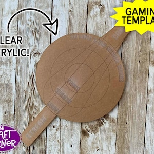 May include: A clear acrylic gaming template with a circular design and a handle. The template has etched lines and the words "Gaming Template" in a yellow starburst. The words "Clear Acrylic!" and "Mini Craft Corner" are also visible.