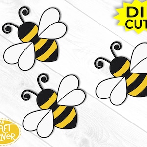 May include: Three die-cut bee shapes with black and yellow striped bodies, white wings, and black antennae. The words "DIE CUTS" are in a yellow starburst. The words "MINI CRAFT CORNER" are in a yellow oval.