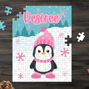 May include: A personalised jigsaw puzzle with a cartoon penguin in a pink hat, scarf, and boots. The name "Desiree" is written in pink script above the penguin. The puzzle is set against a winter scene with snowflakes. Includes a "PNG file" graphic.
