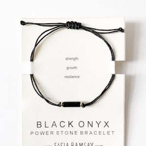 May include: Black onyx power stone bracelet on a white card with the words "strength, growth, resilience" and "BLACK ONYX POWER STONE BRACELET www.SOFIA RAMSAY.com"