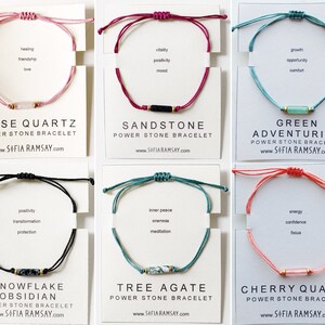 May include: Six different coloured string bracelets with a single stone bead in the centre. The bracelets are labelled with the stone name and the words "Power Stone Bracelet". The website address "www.SOFIA RAMSAY.com" is printed below each bracelet.