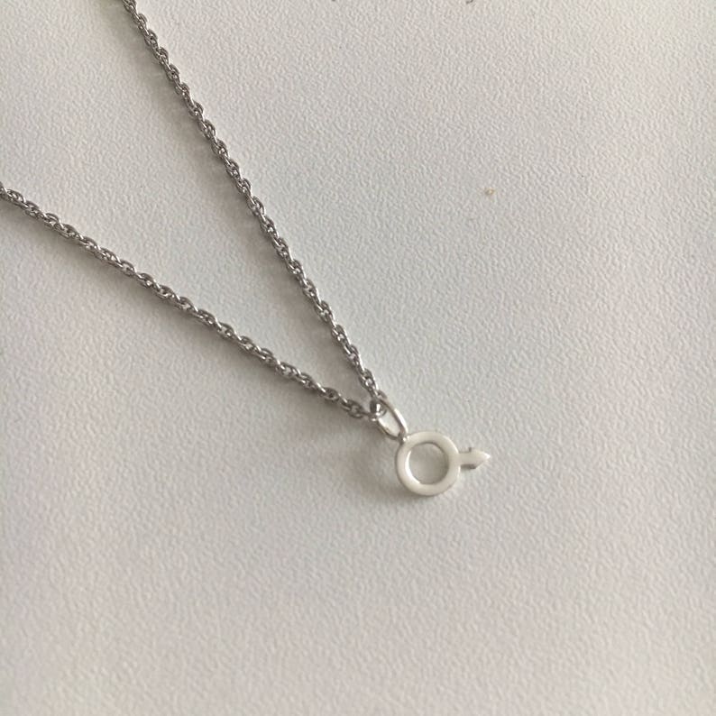 May include: A silver chain necklace with a small silver pendant in the shape of the male symbol.