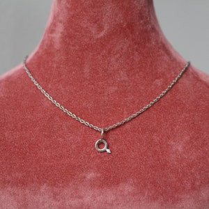 May include: A silver chain necklace with a small silver pendant shaped like a circle with an arrow pointing to the right.
