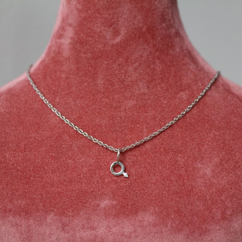 May include: A silver chain necklace with a small silver pendant shaped like a circle with an arrow pointing to the right.