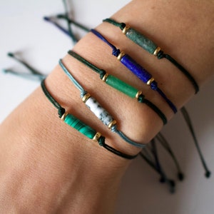 May include: Five bracelets with green, blue and white stones on black string. The stones are all rectangular and have gold beads on either side.
