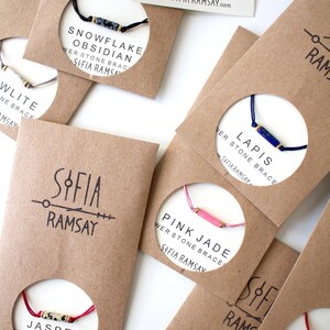 May include: Assortment of colourful bracelets with different gemstone beads and gold accents. Each bracelet is displayed on a brown card with the name of the gemstone and the brand name "Sofia Ramsay".