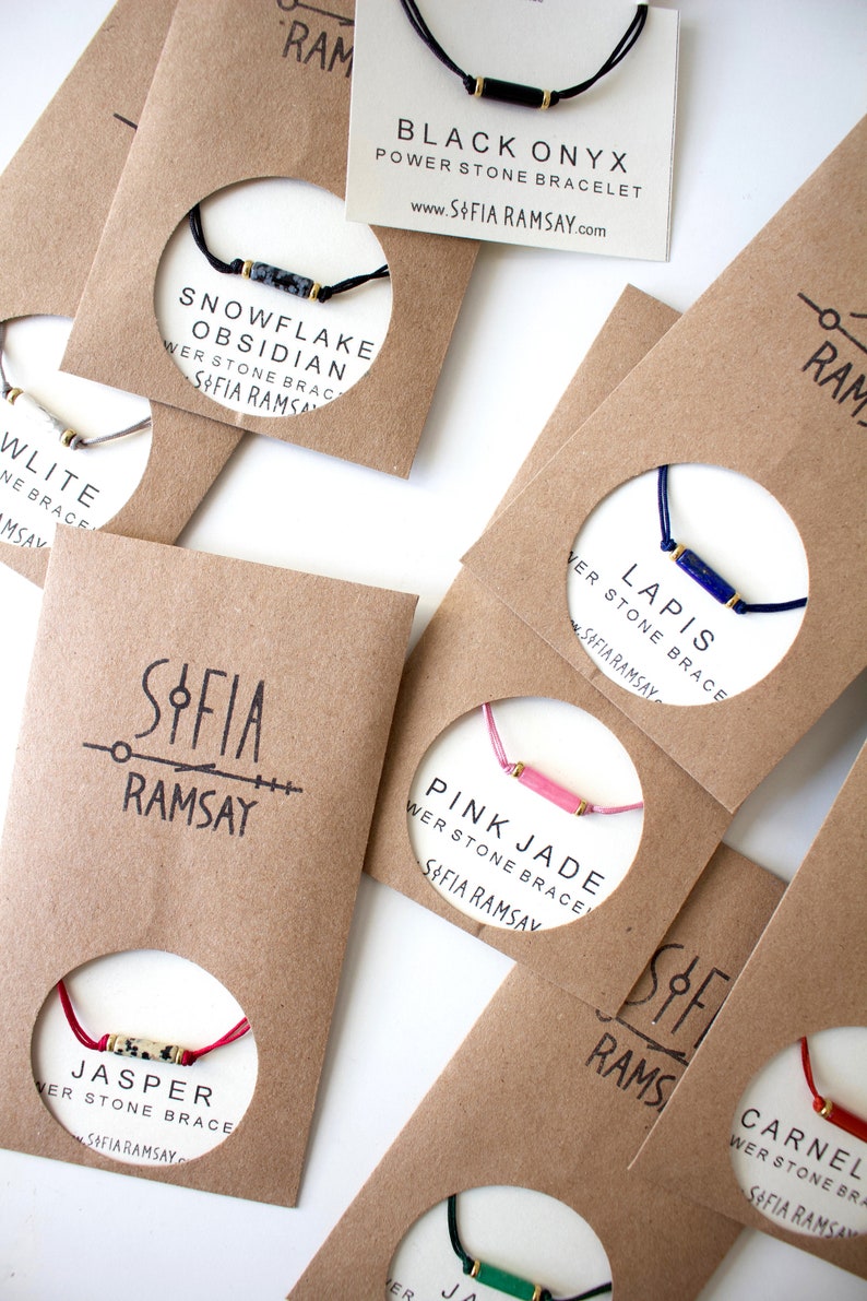 May include: Assortment of colourful bracelets with different gemstone beads and gold accents. Each bracelet is displayed on a brown card with the name of the gemstone and the brand name "Sofia Ramsay".