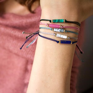 May include: A set of five bracelets with different coloured cords and gemstone beads. The beads are in shades of green, pink, white, and blue.