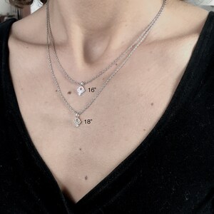 May include: Two silver chains with a small symbol pendant on each. The top chain is 16 inches long and the bottom chain is 18 inches long.