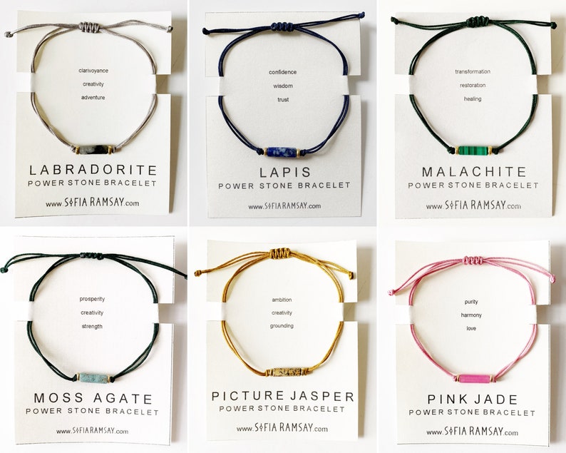 May include: Six different power stone bracelets with various coloured cords and stones. Each bracelet has a card with the stone name, properties, and website address. The stones are Labradorite, Lapis, Malachite, Moss Agate, Picture Jasper, and Pink Jade.