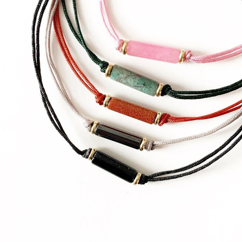 May include: Five bracelets with different coloured cords and gemstone beads. The beads are in shades of pink, green, orange, black, and grey.
