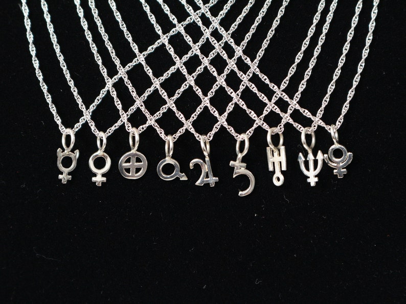 May include: A set of silver necklaces with various celestial symbols as pendants, including the symbols for Venus, Mars, Saturn, Jupiter, Uranus, Neptune, and Pluto.