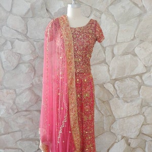 May include: A red and gold embroidered formal dress with a matching pink sheer scarf. The dress features intricate gold detailing and a short-sleeved design. The scarf is draped over the shoulder, adding a touch of elegance.