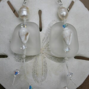 May include: A pair of frosted glass earrings with white pearl accents and crystal beads. The earrings are hanging from silver hooks.