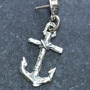 May include: A silver anchor earring with a post. The anchor design has a textured, rustic appearance. The earring is set against a dark grey background.