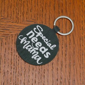 May include: A black round keychain with a silver ring. The keychain has white text that reads "Special needs mama".