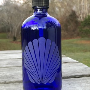 May include: A cobalt blue glass bottle with a black pump dispenser. The bottle has a frosted seashell design etched into the front.