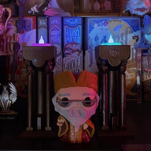 Puede incluir: Una colección de artículos temáticos de Harry Potter, que incluye libros, figuras y candelabros decorativos. La pieza central es una figura Funko Pop de Dumbledore. La escena está iluminada por una suave iluminación colorida, creando una atmósfera mágica.