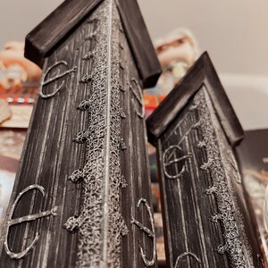 May include: Two tall, black wooden towers with intricate white designs and a pointed top. The towers have a weathered look and are decorated with a repeating pattern of circles.