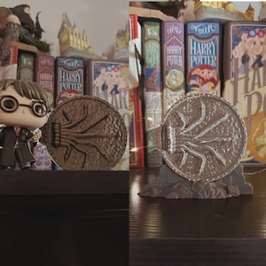 Peut inclure: Un arrêt de porte en forme de saule cogneur, en brun et argent, sur le thème d'Harry Potter. L'arrêt de porte est posé sur une étagère en bois avec une série de livres Harry Potter en arrière-plan.