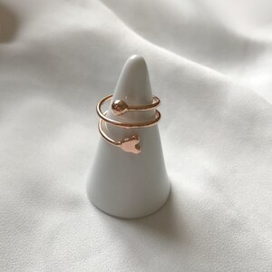 K&ouml;nnte beinhalten: Ein Set aus drei goldfarbenen Ringen mit einem Herz- und einem Kugeldesign. Die Ringe werden auf einem wei&szlig;en, kegelf&ouml;rmigen Ringst&auml;nder pr&auml;sentiert.