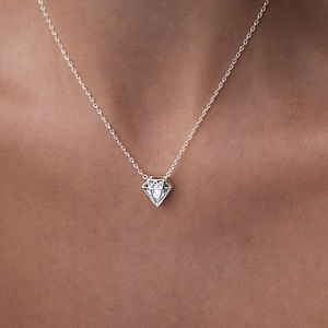 Op de afbeelding: Een zilveren ketting met een diamantvormige hanger en een heldere, facetgeslepen middensteen. De hanger hangt aan een delicate ketting. De ketting wordt getoond tegen een neutrale achtergrond.