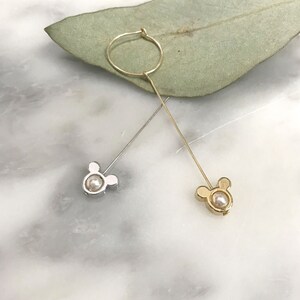 May include: A pair of dangle earrings with a pearl and a Mickey Mouse head design. One earring is gold and the other is silver.