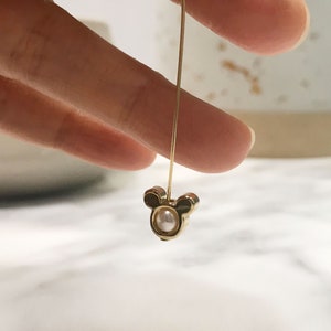 May include: Gold dangle earring with a pearl and Mickey Mouse head design.