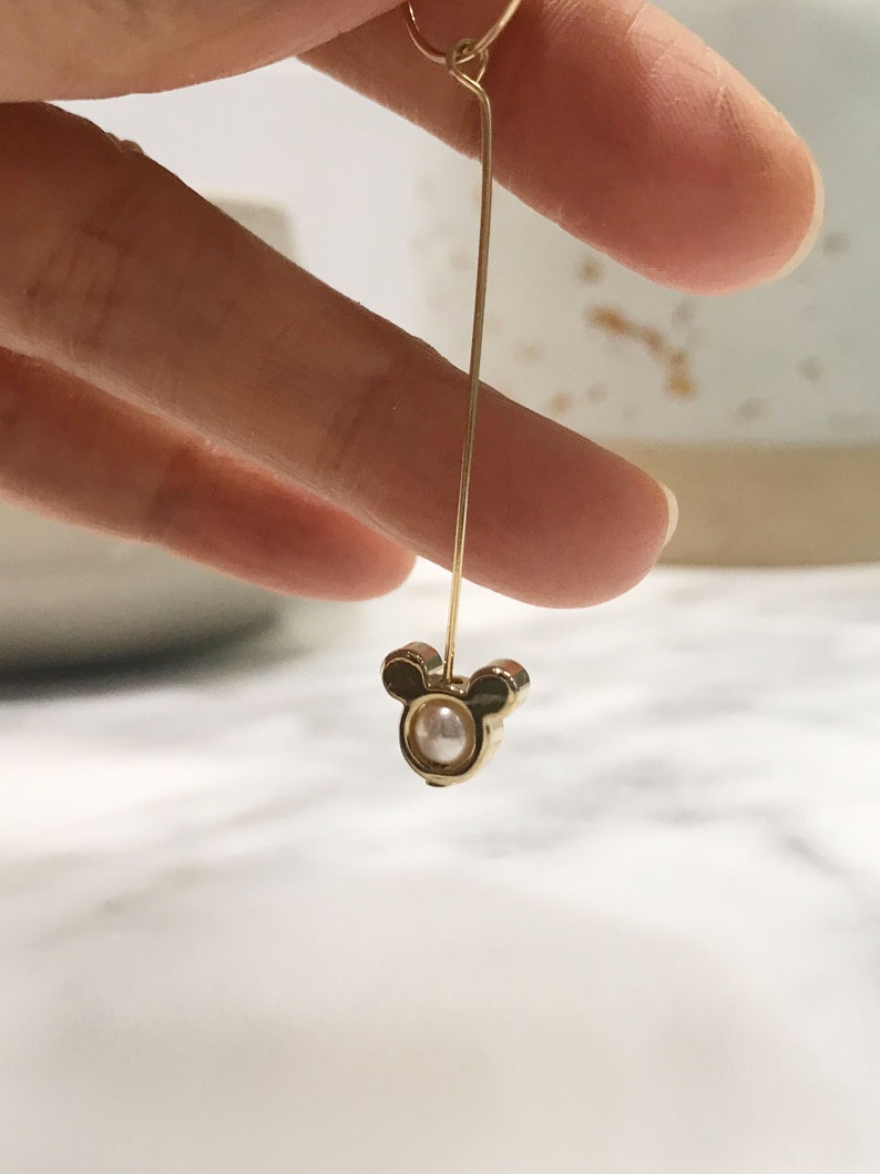 May include: Gold dangle earring with a pearl and Mickey Mouse head design.