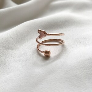 K&ouml;nnte beinhalten: Ein Ring aus Ros&eacute;gold mit einem herzf&ouml;rmigen Design und einer kleinen Kugel am Ende des Bandes.