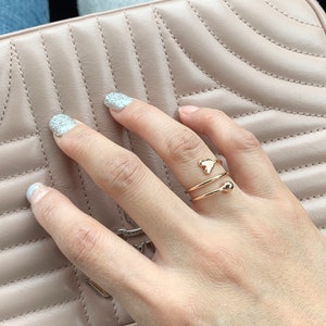 K&ouml;nnte beinhalten: Ein goldener Ring mit einem herzf&ouml;rmigen Design und einer kleinen Kugel an der Band.