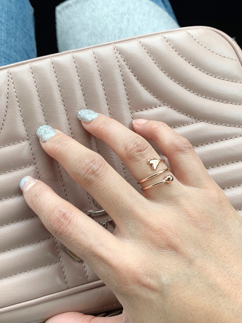 K&ouml;nnte beinhalten: Ein goldener Ring mit einem herzf&ouml;rmigen Design und einer kleinen Kugel an der Band.