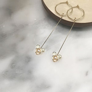 May include: A pair of gold hoop earrings with a dangling pearl and a small Mickey Mouse charm.