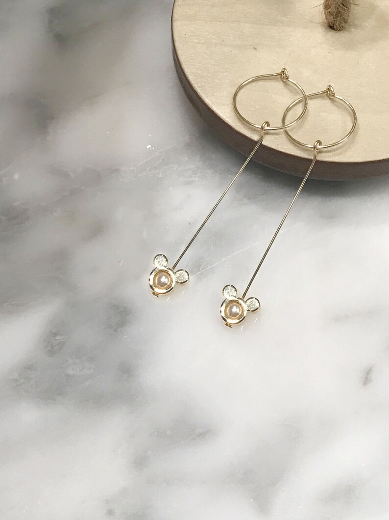 May include: A pair of gold hoop earrings with a dangling pearl and a small Mickey Mouse charm.