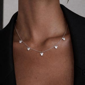 May include: Silver necklace featuring multiple small, stylized mouse head charms. The delicate chain is worn around the neck, with the charms evenly spaced. The necklace is a simple yet elegant piece of jewelry.