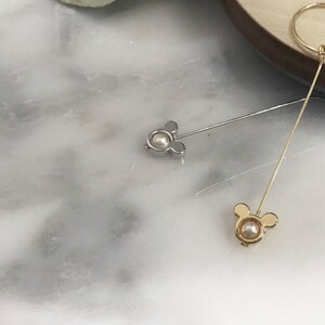May include: Two gold and silver earrings with a pearl in the center and a Mickey Mouse design.