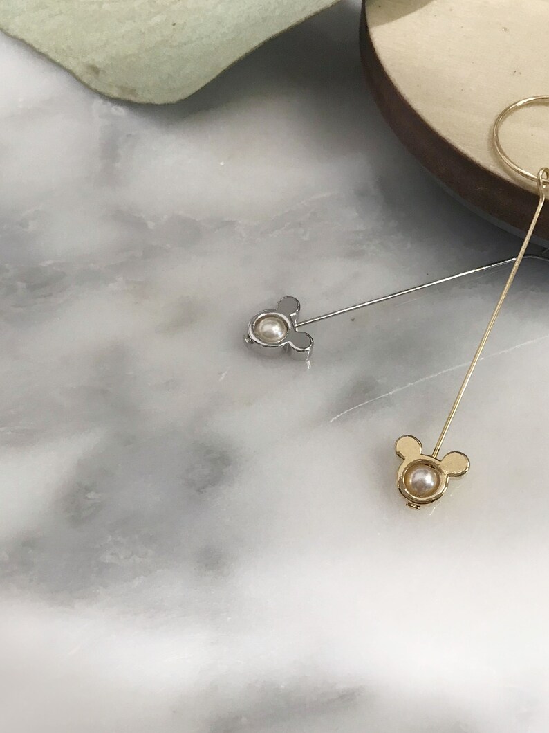 May include: Two gold and silver earrings with a pearl in the center and a Mickey Mouse design.