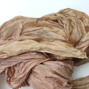 May include: A soft, sheer scarf in shades of brown and beige. The scarf is made of silk and has a delicate, flowing texture.