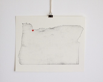 May include: A black and white print of the state of Oregon with a red heart marking a location on the map.
