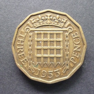 May include: A bronze-colored British three pence coin with the royal coat of arms and the year 1953.